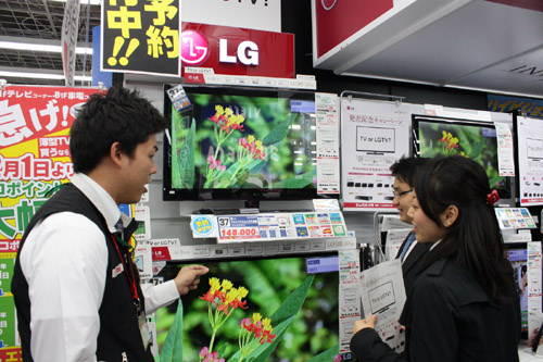 A man explains LG’s LED LCD TVs to two visitors at an LG store booth set up in Japan.