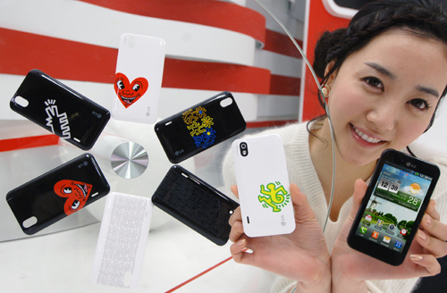 A model holds up two LG Optimus Black phones, showing off the front and rear of the device while next to 6 different back cover designs from the Keith Haring Foundation.