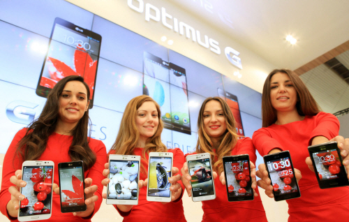 Four female models are smiling at a camera holding various strategic Optimus series devices at MWC 2013 - G, Vu:, F and LII.