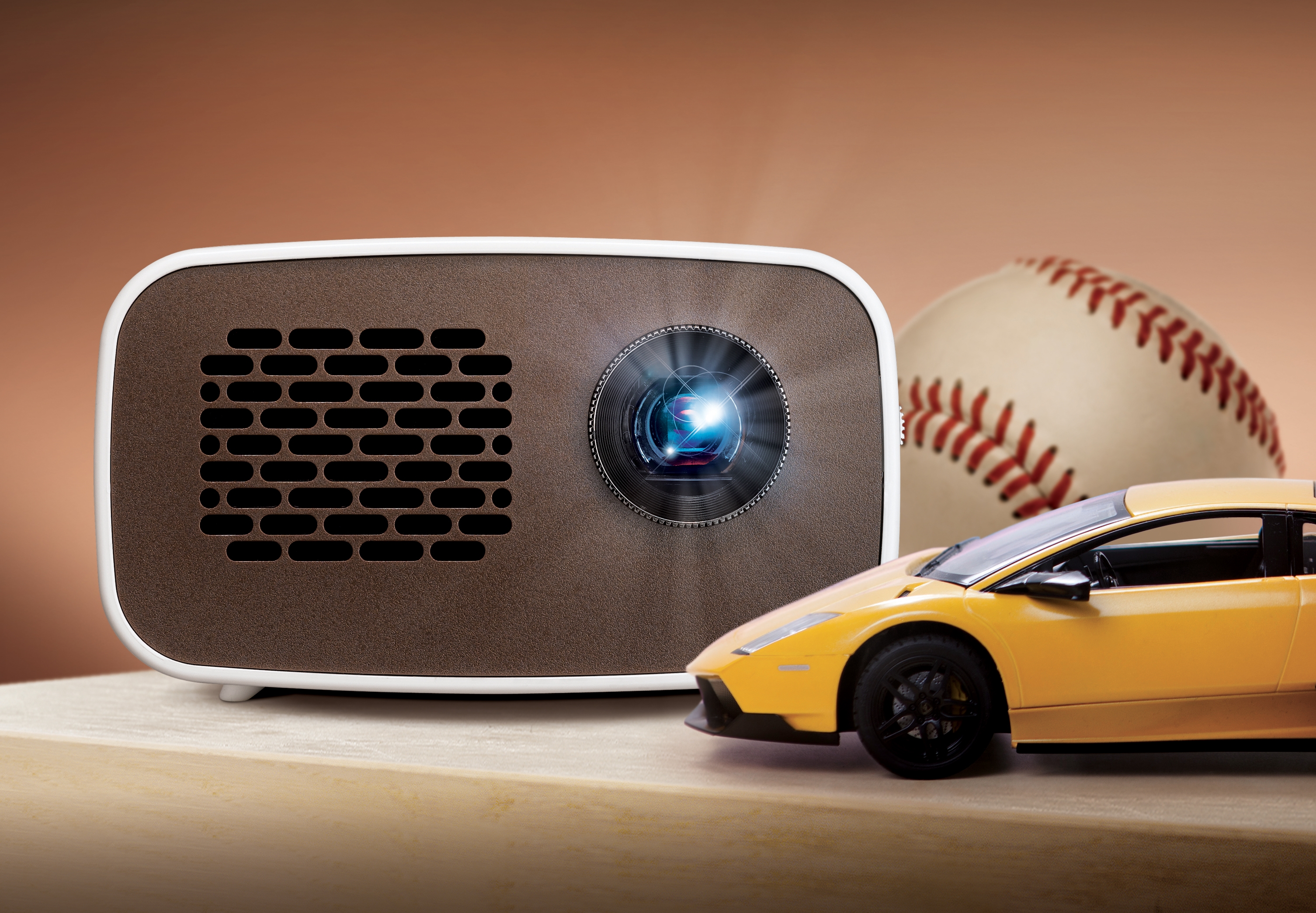 Front view of LG HD MiniBeam model PH300 beaming light on a table next to images of a baseball and supercar