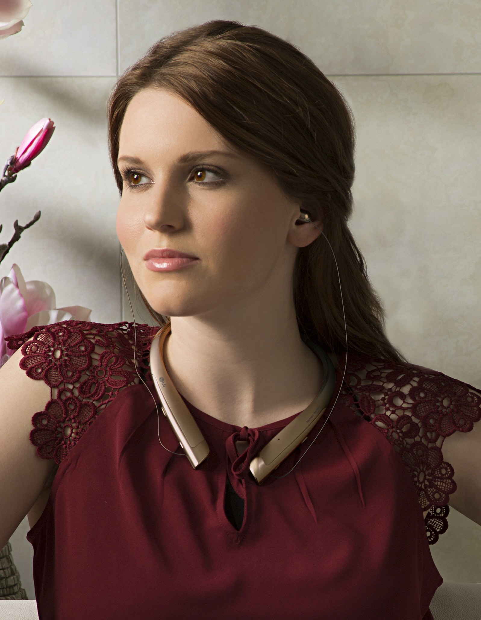A woman with the LG TONE Platinum™ in Gold around her neck and the retractable ear buds in her ears