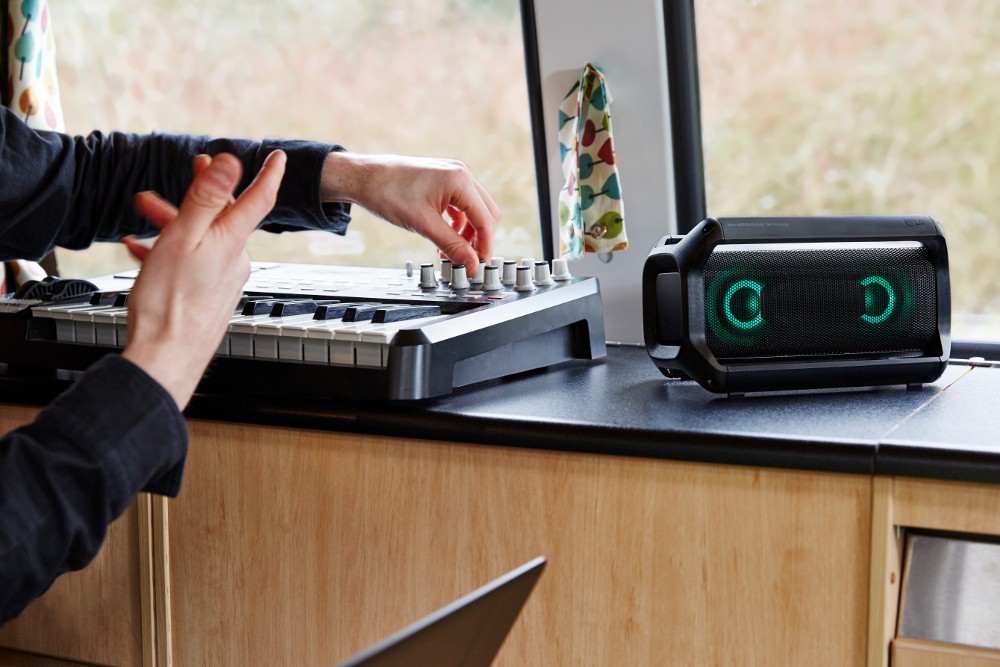 Someone controls a music device next to an LG XBOOM Go