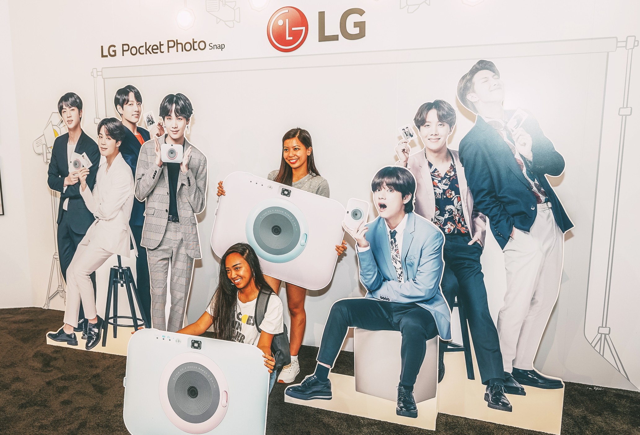 Visitors take a picture at the LG Pocket Photo Snap booth with cutouts of their favorite K-pop group.