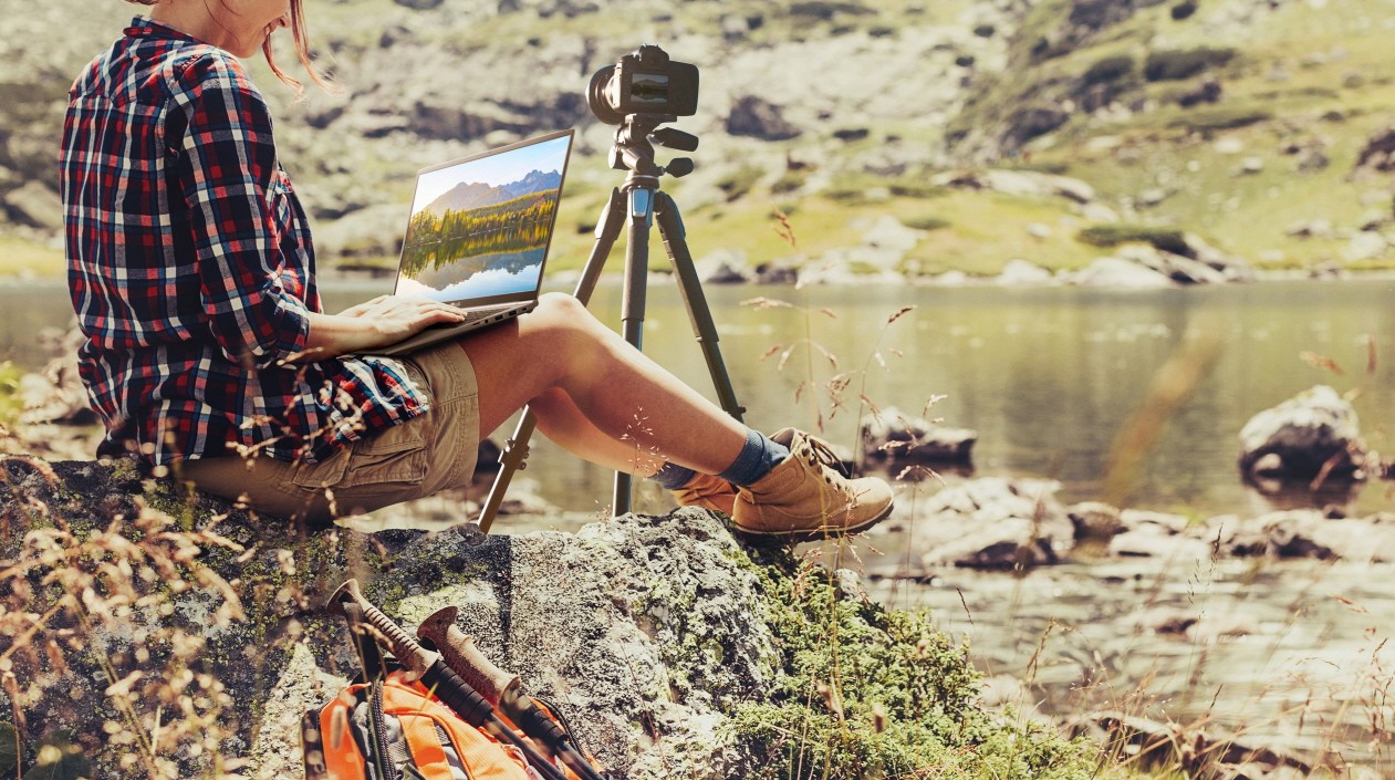 A lady working on pictures with her LG gram while sitting on a rock beside the river