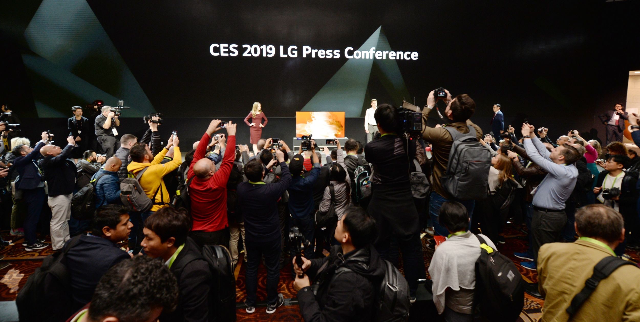 David VanderWall, Senior Vice President of Marketing at LG Electronics USA and Tim Alessi Senior Director of Product Marketing for Home Entertainment Products at LG Electronics USA are onstage discussing the LG SIGNATURE OLED TV R at LG's CES 2019 Press Conference while a number of reporters take pictures of the TV.