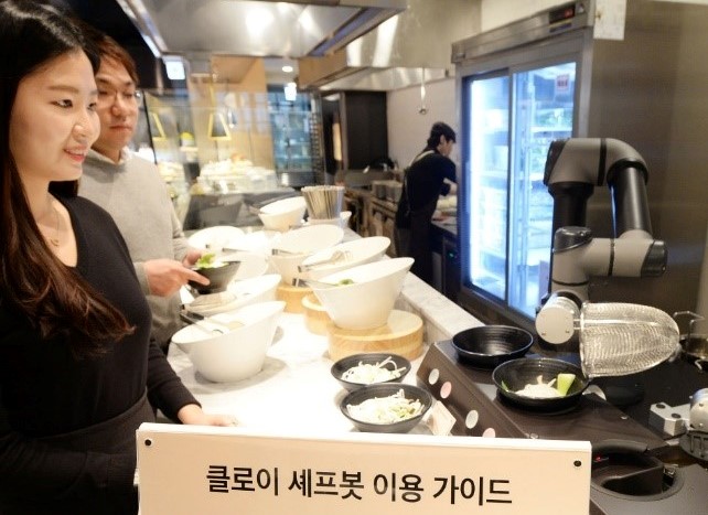 A man and women at a buffet being served their meals by LG ChefBot