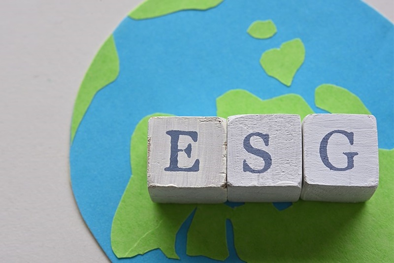 Three cubes displaying letters from the acronym ESG stand on top of a handmade picture of the world.