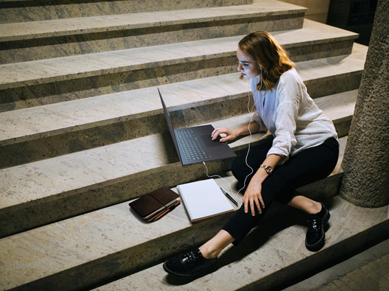 A woman casually sitting down on the stairs while working with her LG gram and a notebook.