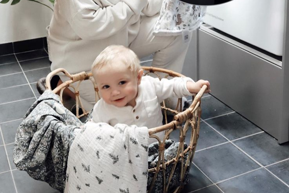 A woman using an LG washing machine to do her laundry as her baby plays inside the clothes basket.